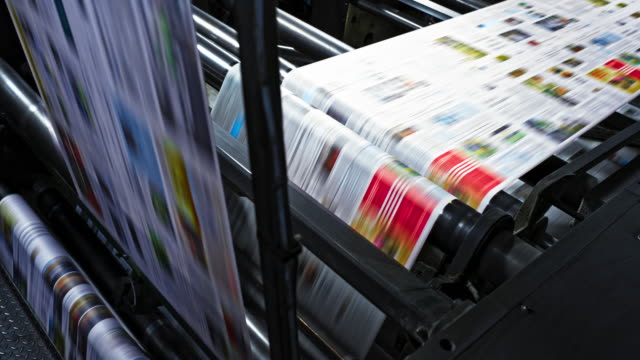 Medium high angle locked down shot of the colorful paper travelling across the printing press in the printing factory. Shot in Slovenia.